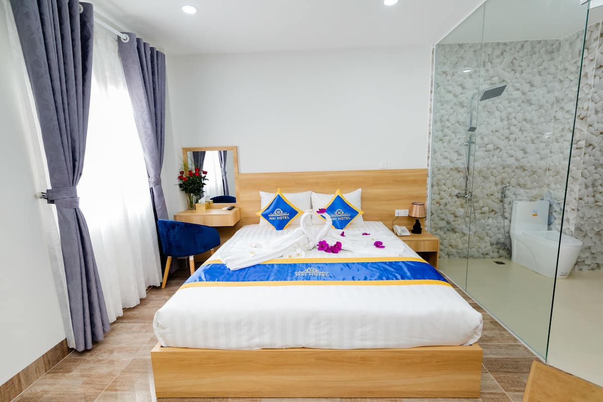 Ein Hotelzimmer mit einem großen Bett, einem Holzkopfteil, einem Nachttisch, einem Spiegel und einer Duschkabine aus Glas.
