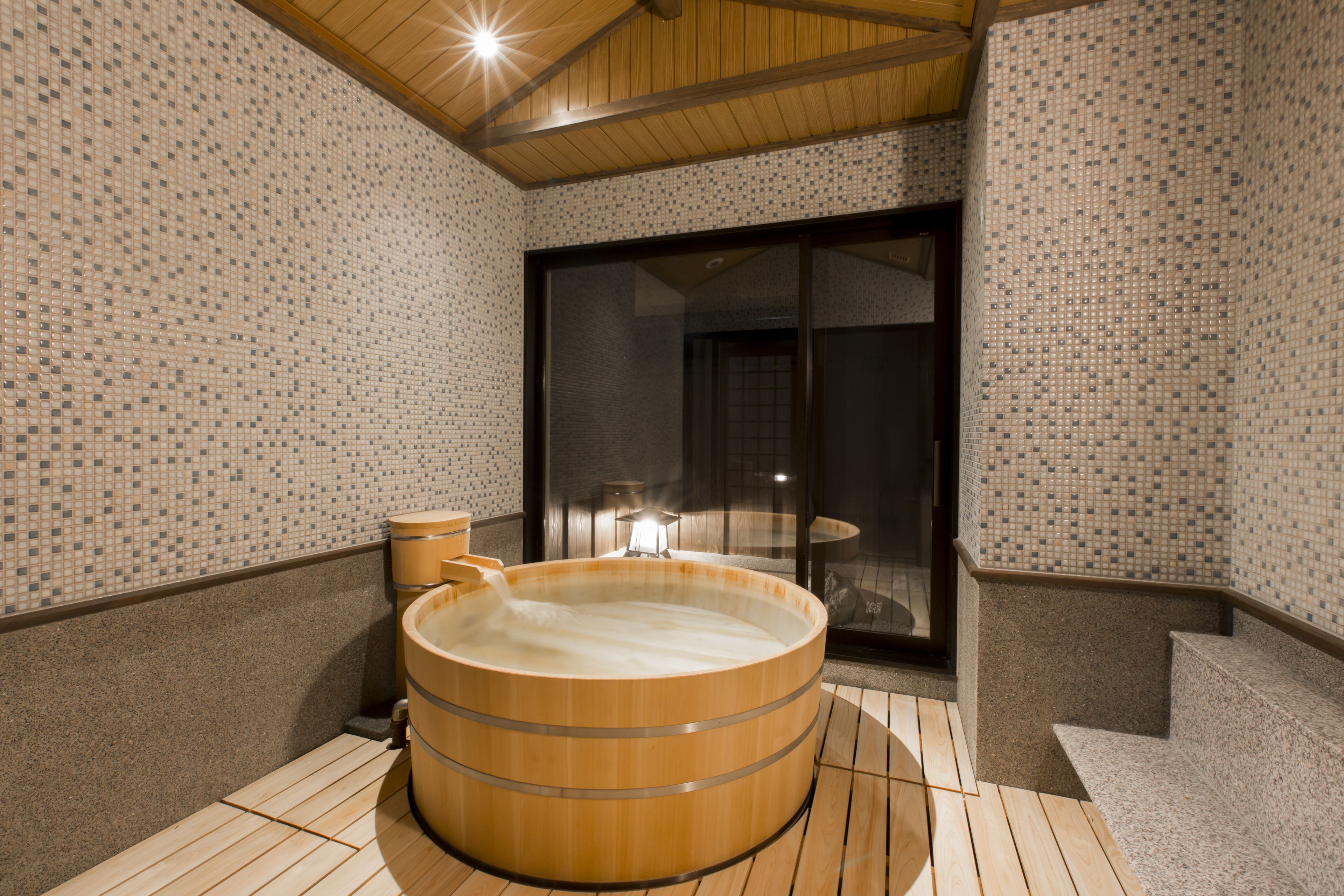 A traditional Japanese-style room with tatami flooring, a wooden hot tub, and a sliding glass door leading to a balcony.