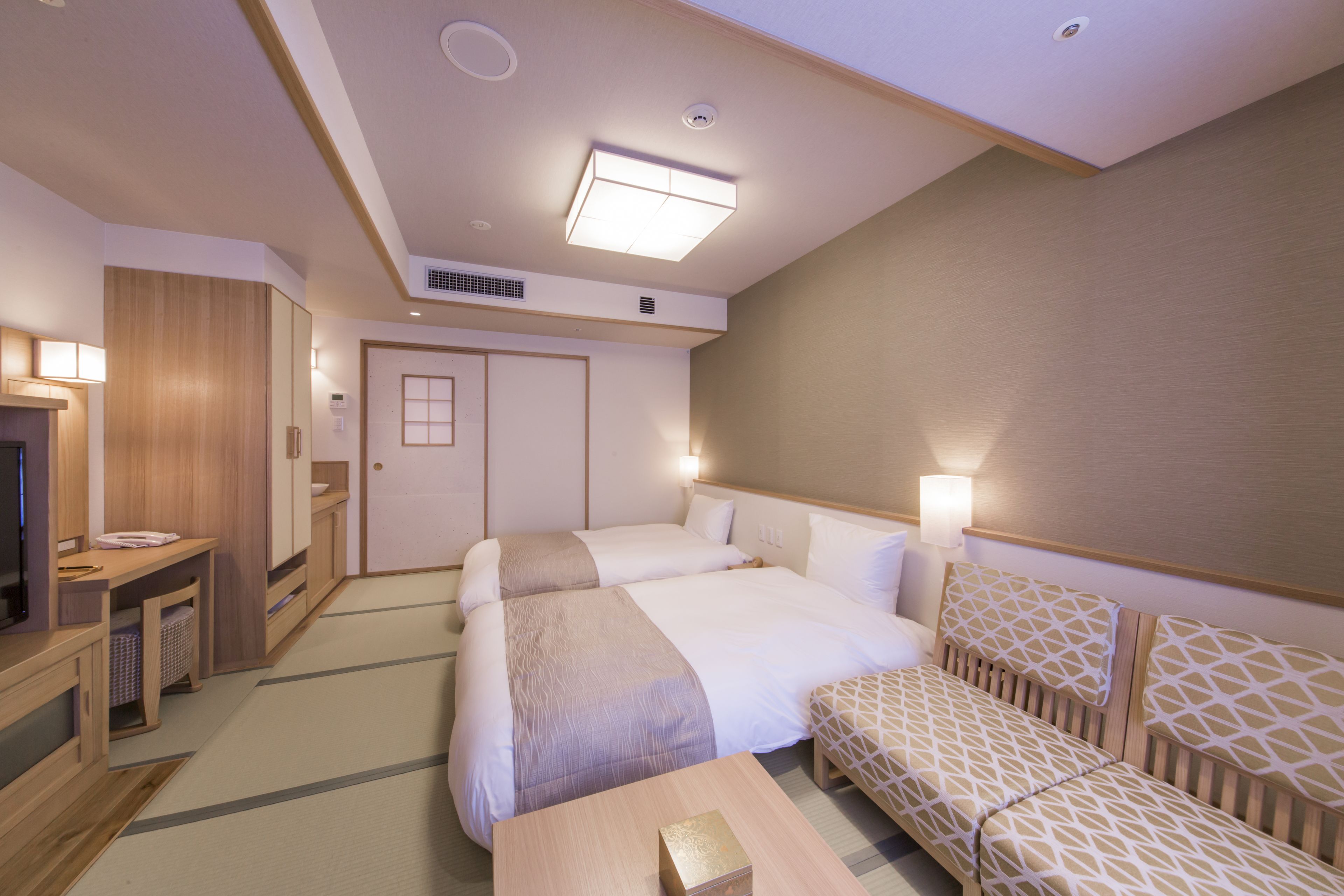 A hotel room with a bed, bedside tables, a TV, and a sofa.