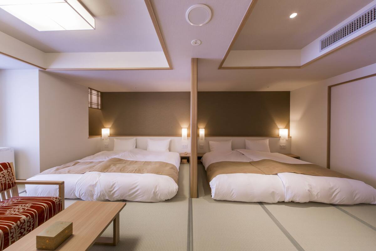 A hotel room with two beds, a wooden bench, and a small table.
