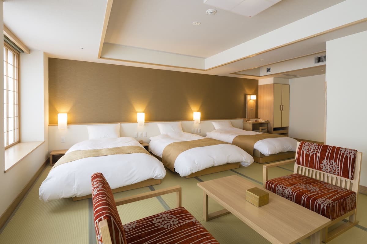 A hotel room with three beds, a sofa, a small table, and a mirror.