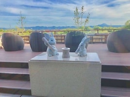 Una terraza con dos macetas grandes y oscuras y dos esculturas de conejos blancos sobre un pedestal blanco.