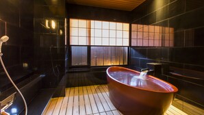 A modern bathroom with a wooden floor, a large red bathtub, and a glass shower enclosure. - Oyado Tsukiyonousagi (Izumo)