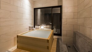 A modern bathroom with a wooden bathtub, tiled walls, and a glass door leading to a shower area. - Oyado Tsukiyonousagi (Izumo)