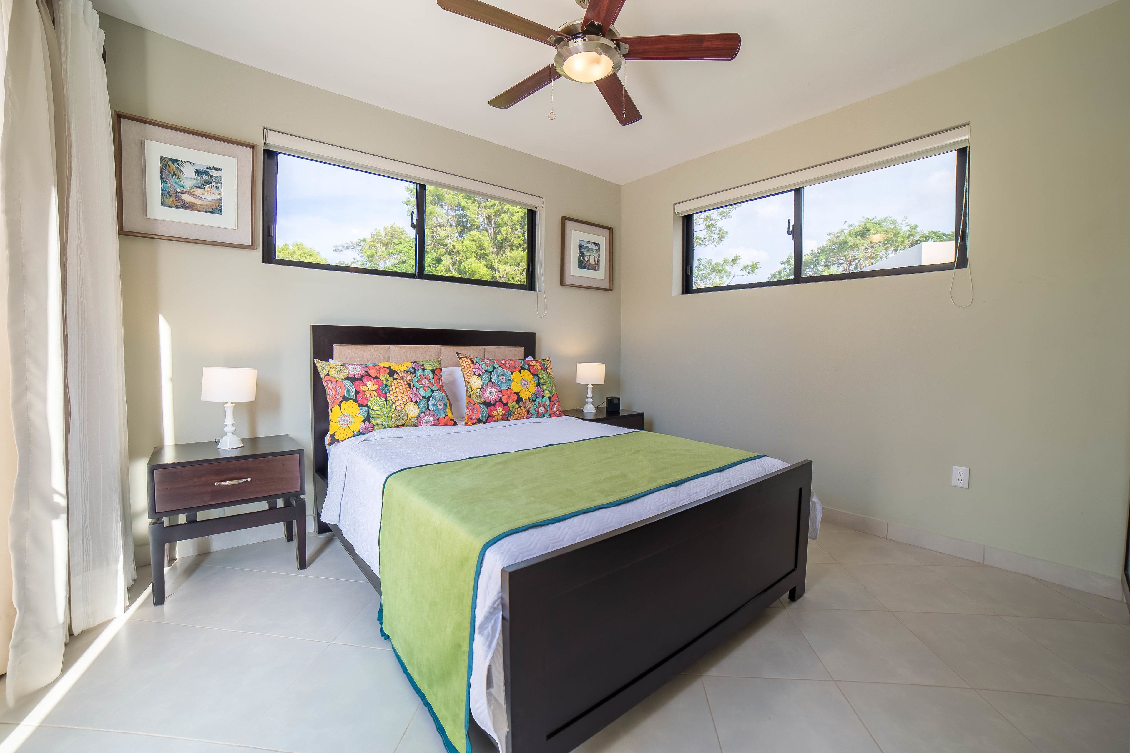 A bedroom with a bed, two bedside tables, a ceiling fan, and two windows.