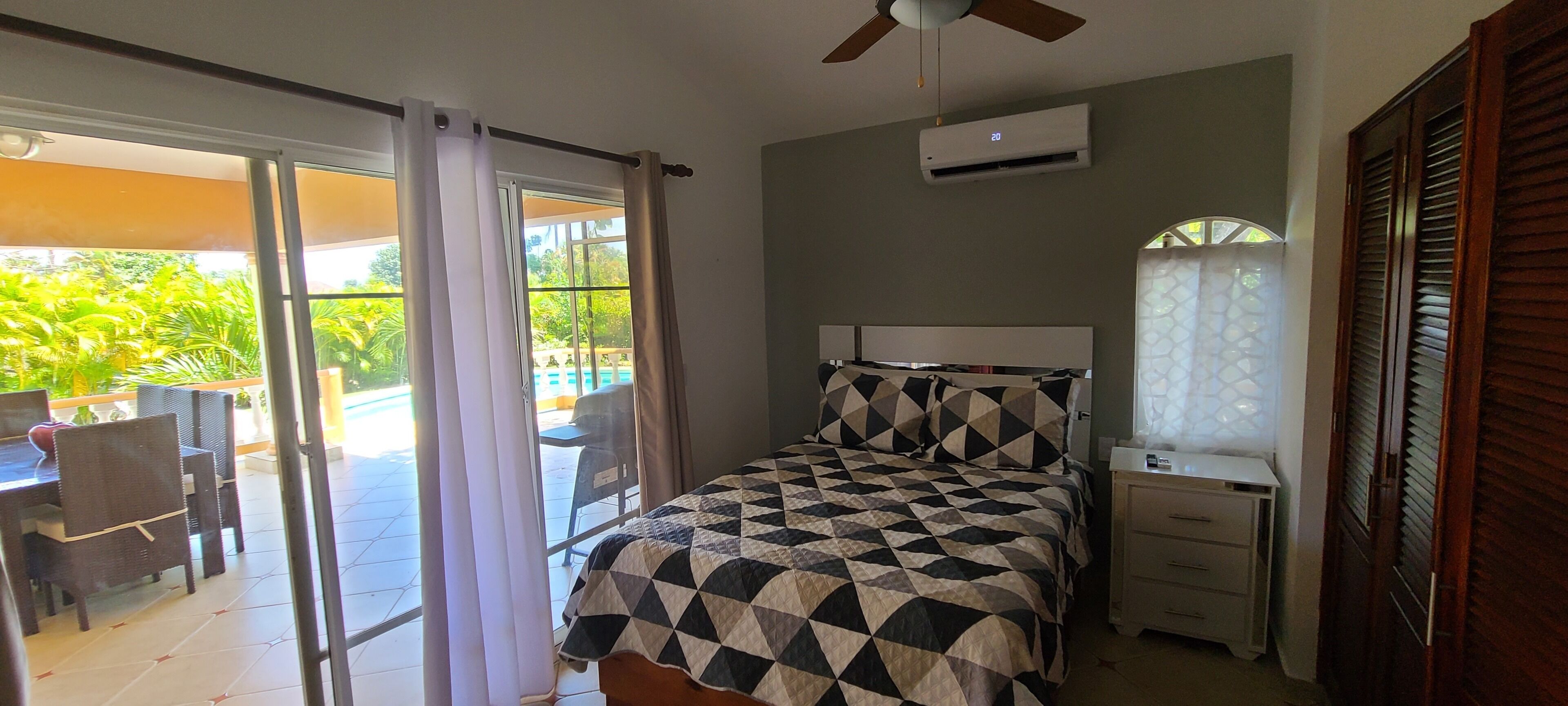 Un dormitorio con una cama, una mesita de noche, un ventilador de techo y un equipo de aire acondicionado.