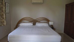 Un lit bien fait, avec une tête de lit en bois, un climatiseur fixé au mur et une armoire en bois fermée.