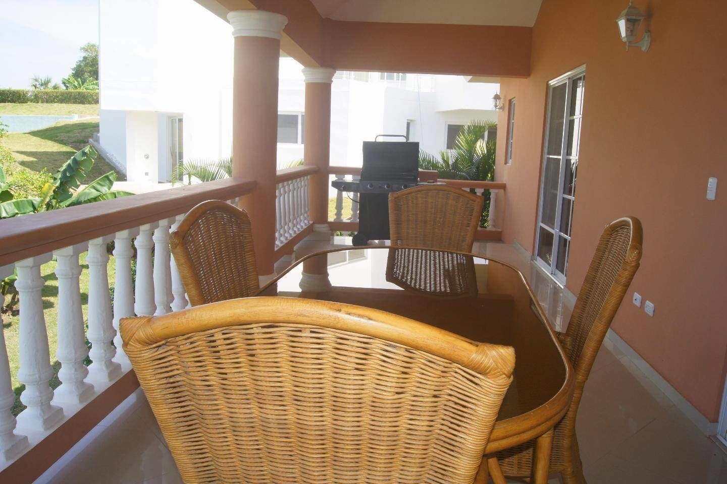 A balcony with wicker furniture, a grill, and a view of the outdoors.