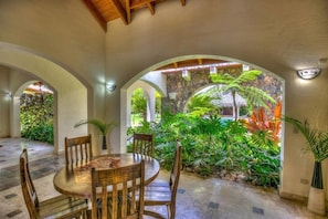 A dining area with a round table and chairs, surrounded by arches and lush tropical plants. - Casa Las Brisas A Caribbean Vacation Dream (Cabarete)