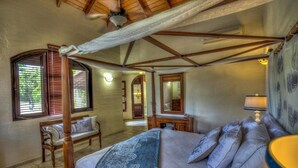 A bedroom with a bed, a bedside table, a lamp, a window with blinds, and a ceiling fan. - Casa Las Brisas A Caribbean Vacation Dream (Cabarete)