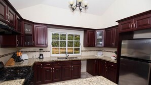 A kitchen with dark wood cabinets, a granite countertop, a stainless steel refrigerator, and a window with a view of greenery.