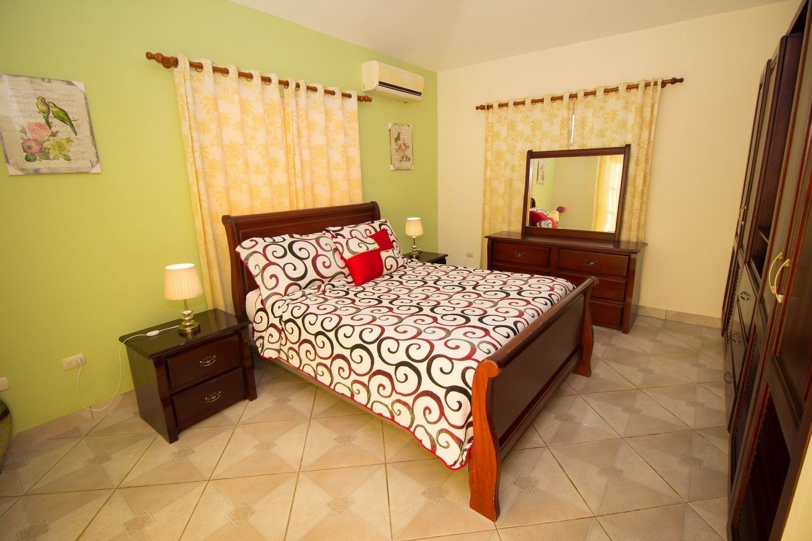 A bedroom with a bed, nightstands, a dresser, a mirror, and a wall-mounted air conditioner.