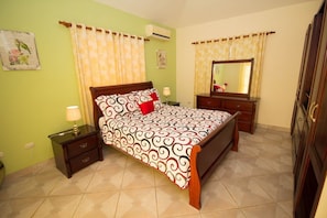 Un dormitorio con cama, mesitas de noche, cómoda, espejo y aire acondicionado instalado en la pared.