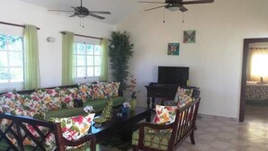 A living room with a sofa, two chairs, a coffee table, a TV, and two ceiling fans.