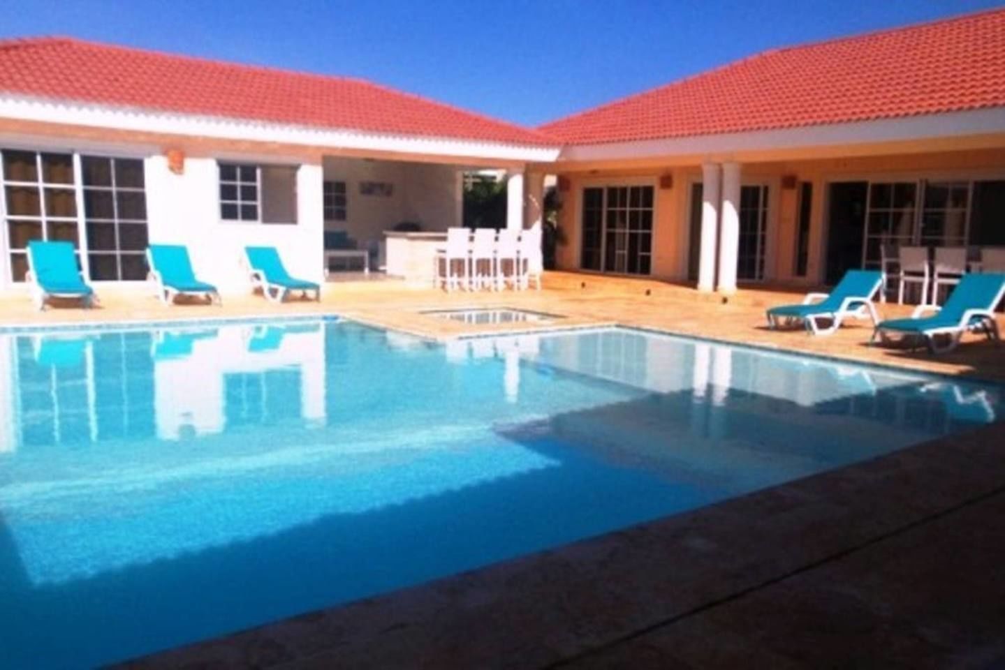 Ein Swimmingpool mit blauem Wasser, umgeben von Liegestühlen und einem Gebäude mit rotem Ziegeldach.