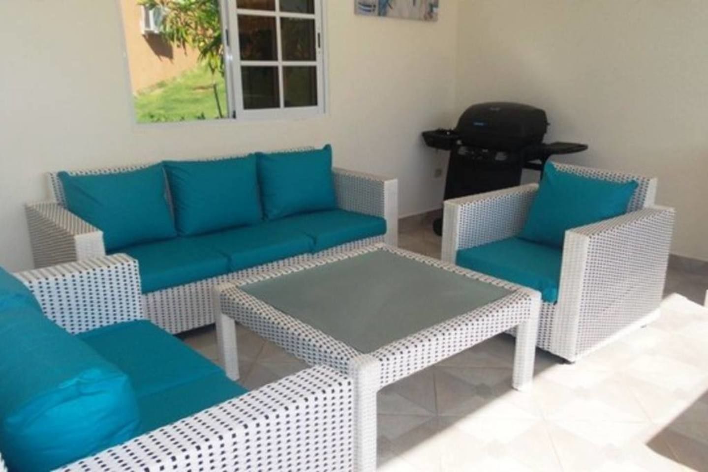 Un espace patio aménagé avec un ensemble de canapés et de fauteuils en osier blanc assortis, une petite table et un barbecue.