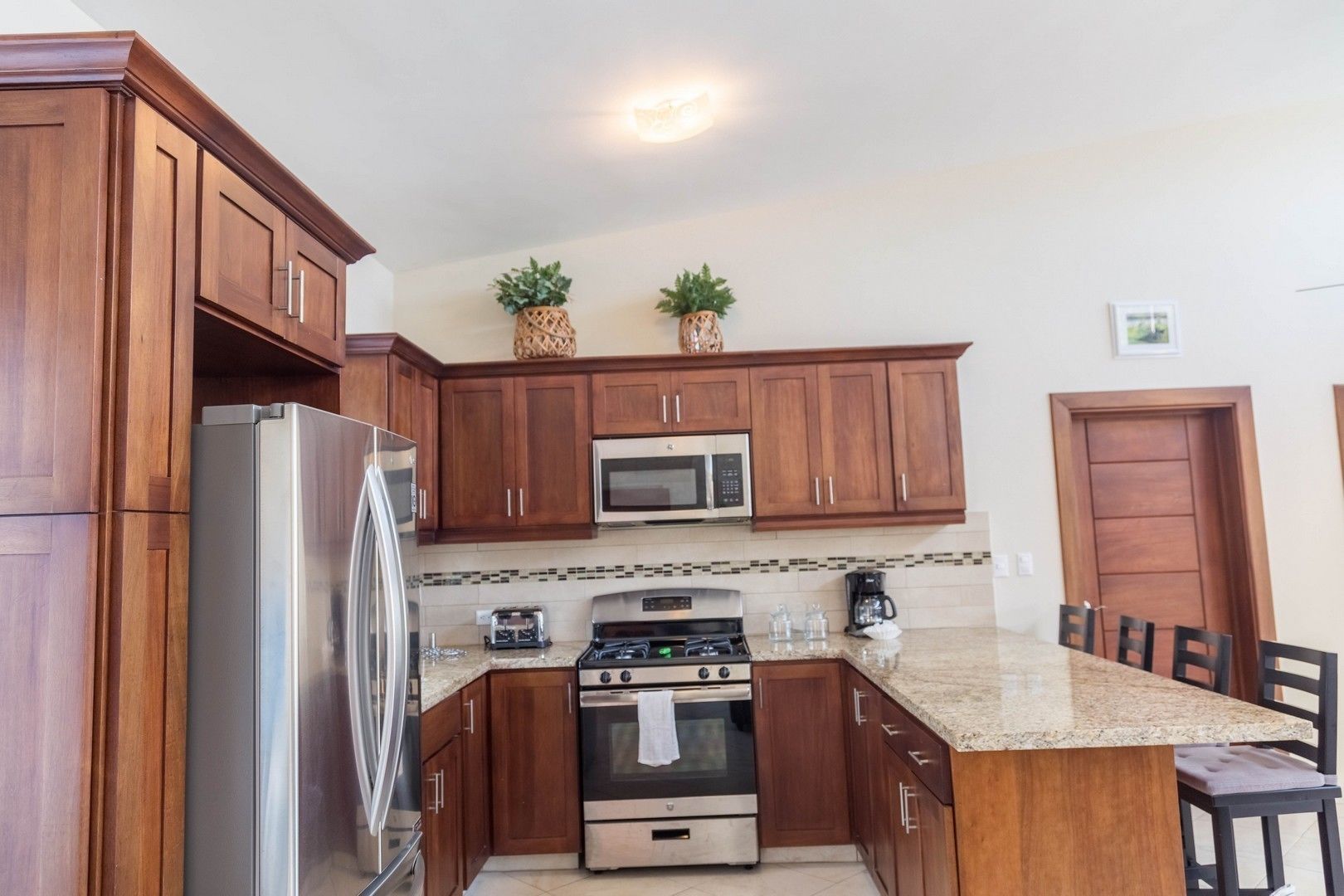 A kitchen with wooden cabinets, stainless steel appliances, a granite countertop, and a dining area with chairs.