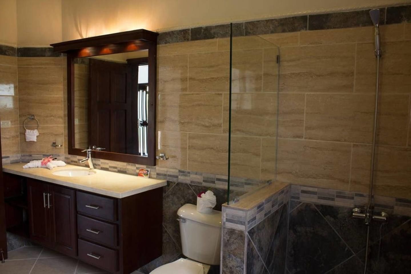 Une salle de bain avec un grand miroir, un lavabo, des toilettes et un espace douche.
