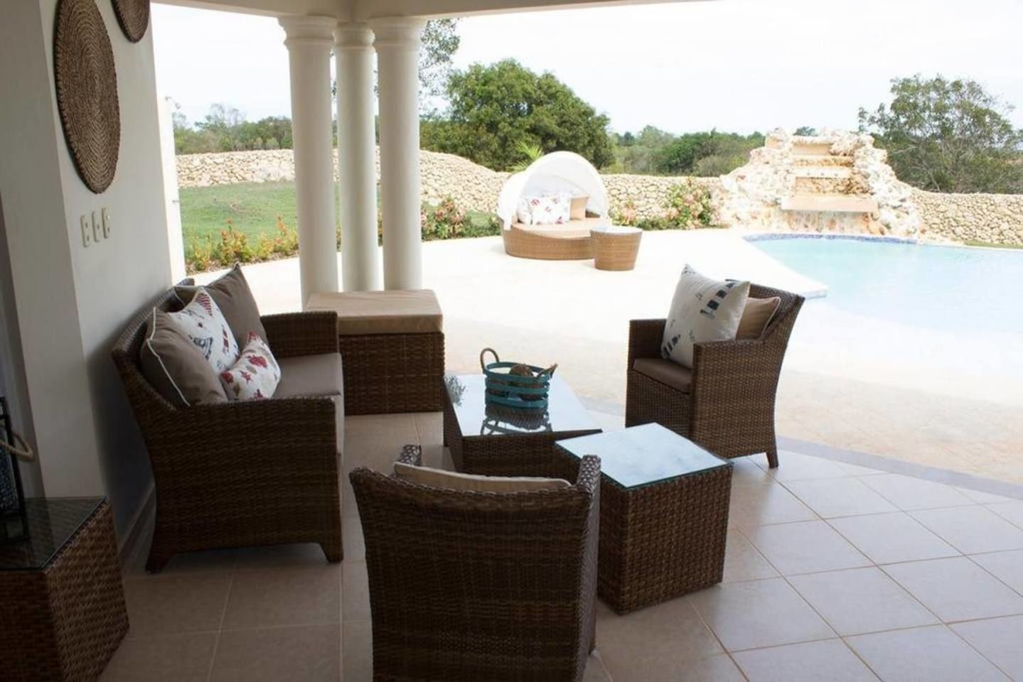 A covered outdoor seating area with wicker furniture and a view of a swimming pool.