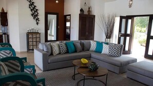 A living room with a grey sectional sofa, teal and patterned armchairs, a coffee table with decorative items, and a large mirror above the sofa. - 4 Bed Villa Minutes From Downtown Sosua (Sosúa)