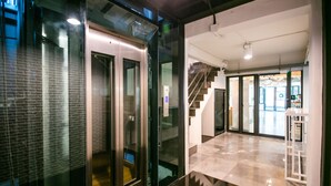 Un interior moderno con un ascensor de vidrio, una escalera y un piso de baldosas limpias.