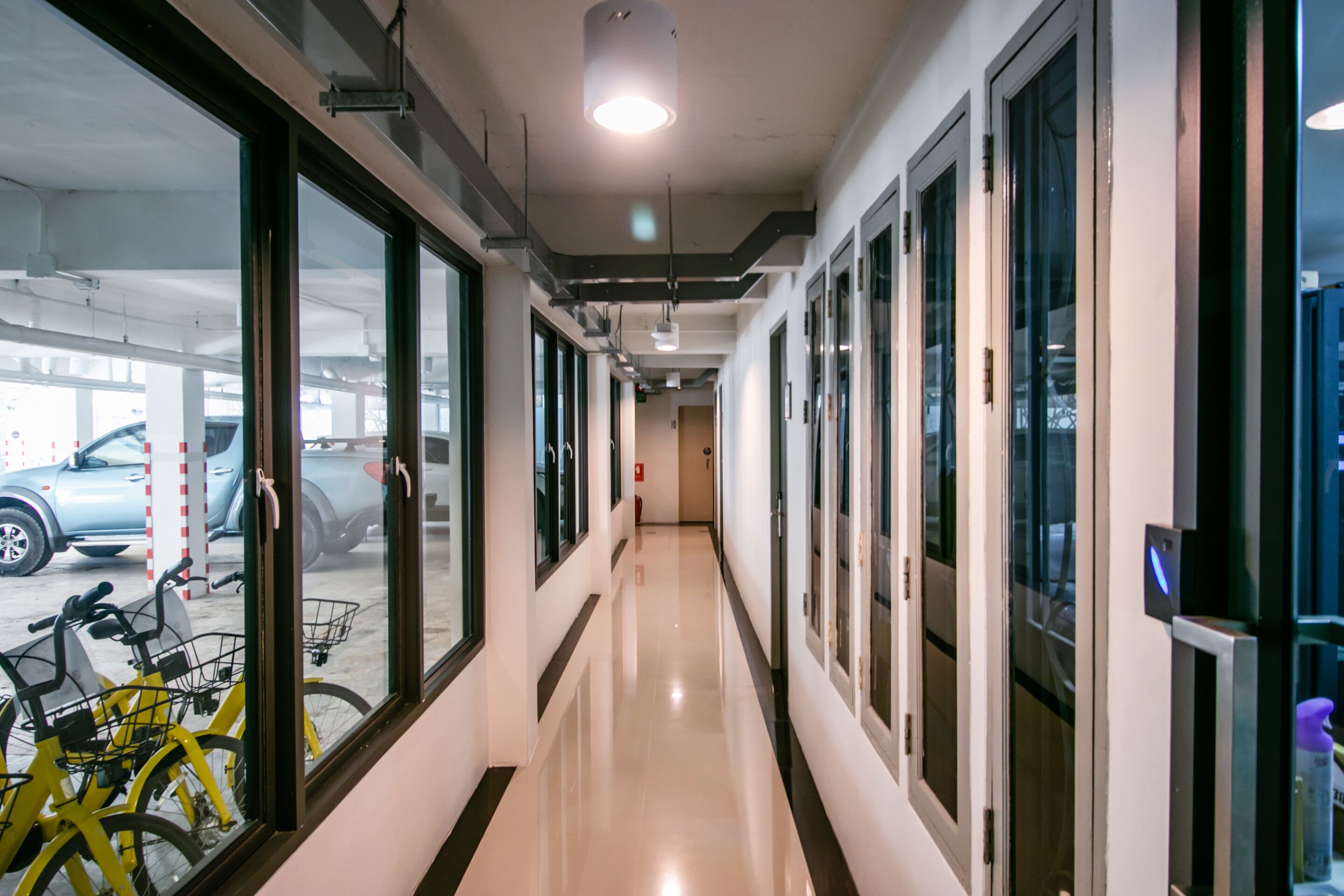 A clean, well-lit hallway with large windows on one side and a parking area visible through the windows.