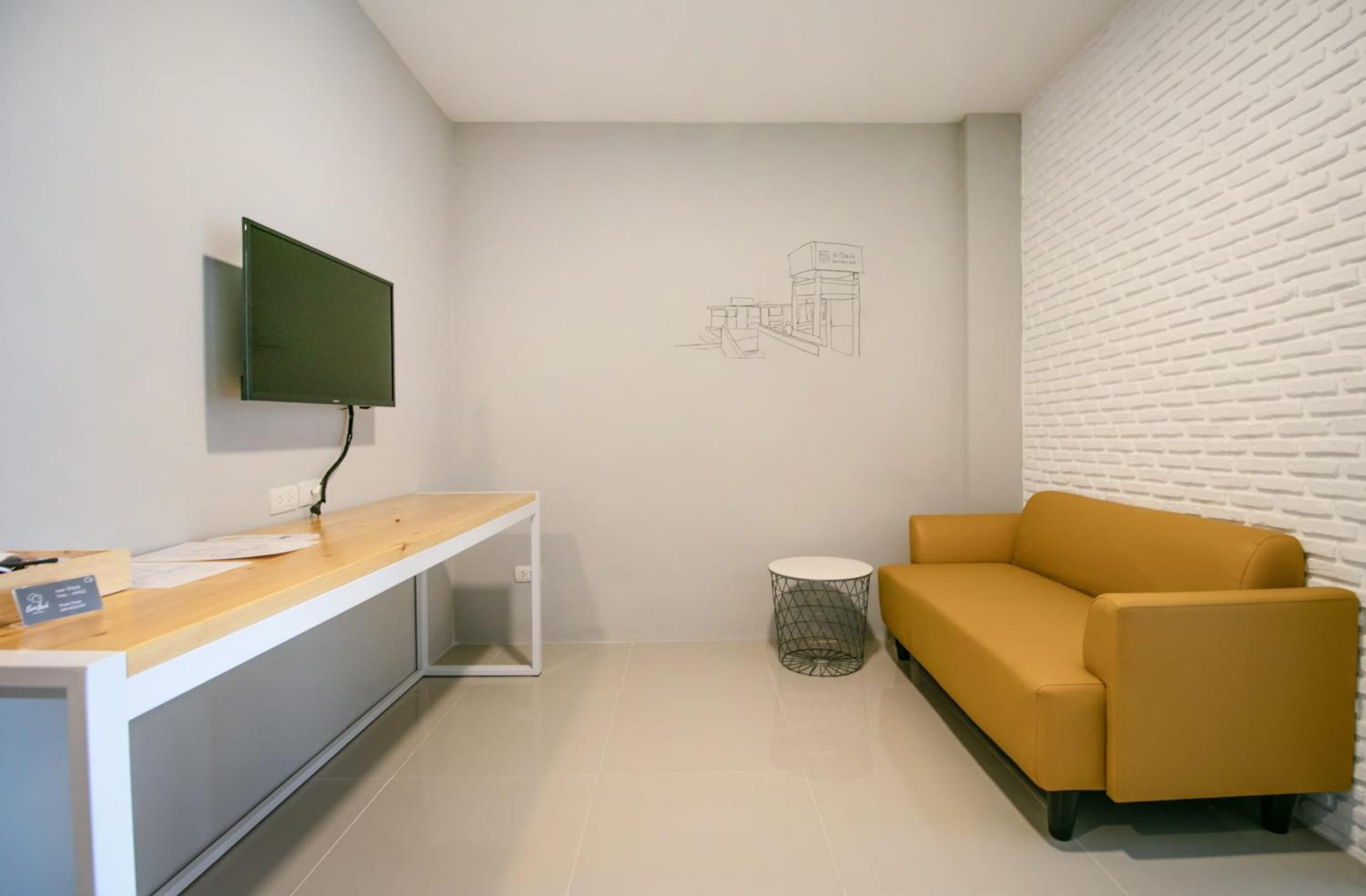 Una habitación moderna con un escritorio de madera, un televisor de pantalla plana, un sofá amarillo y una pared de ladrillo blanco.