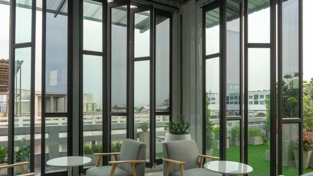 Un espacio interior moderno con amplios ventanales, sillones tapizados de gris y mesitas redondas.