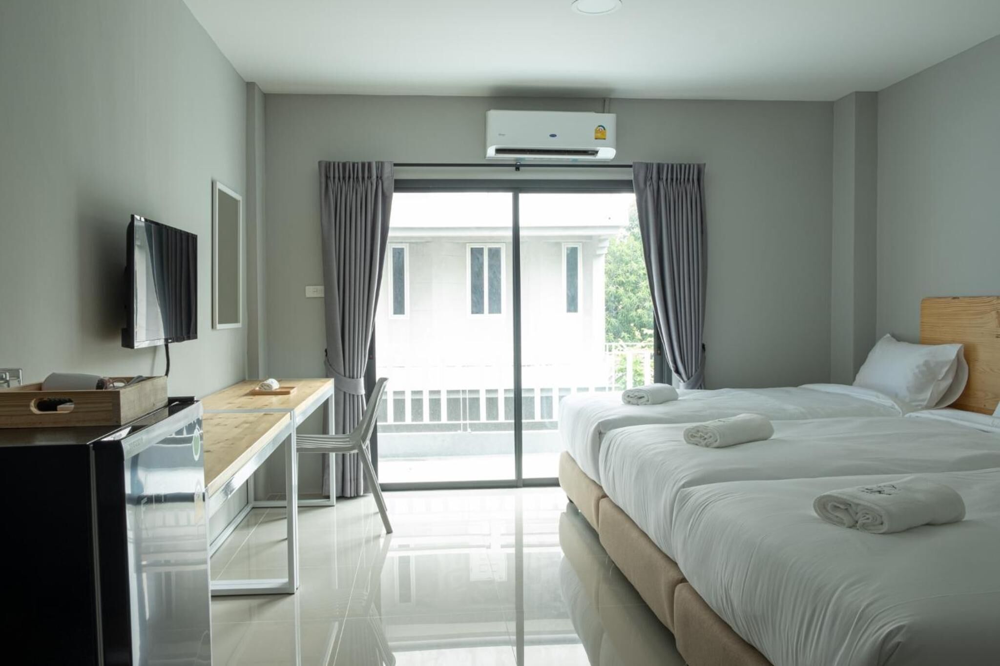 A hotel room with a bed, a desk, a television, and a balcony with curtains.