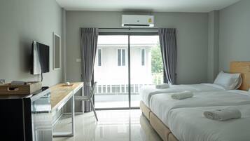 A hotel room with a bed, a desk, a television, and a balcony with curtains.