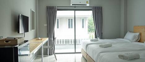 A hotel room with a bed, a desk, a television, and a balcony with curtains.