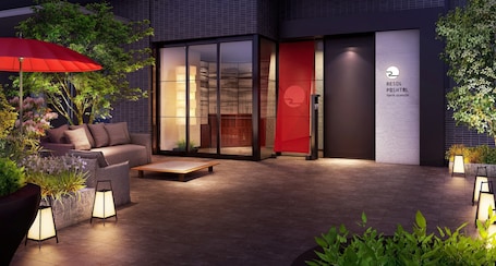 An outdoor seating area with a sofa, a small table, and a red umbrella. There is a sign for the Resid Resort Hotel in Tokyo Asakusa.