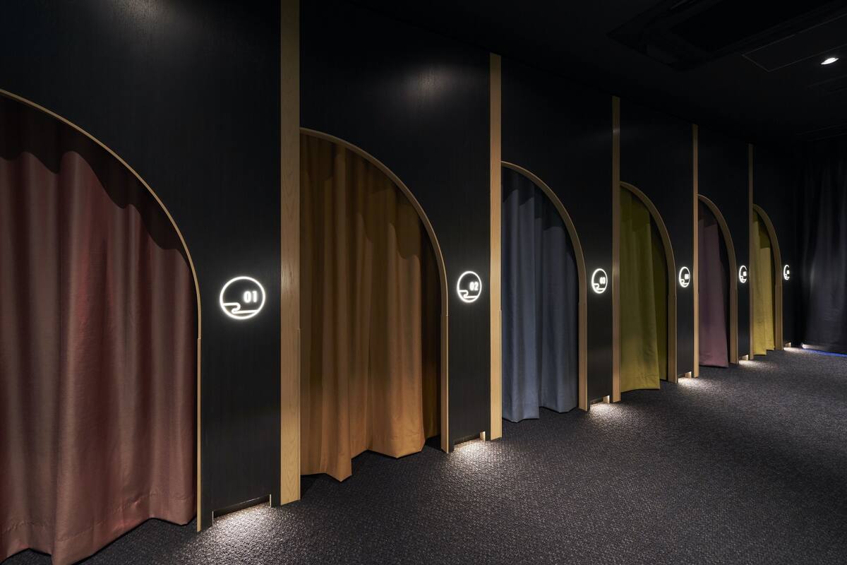 A row of private rooms with individual curtains and illuminated door signs.