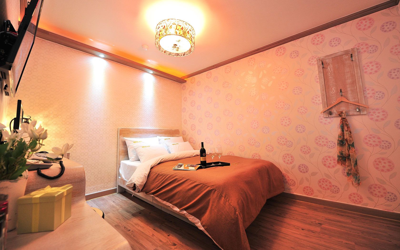 Ein ordentlich eingerichtetes Schlafzimmer mit einem hölzernen Bett, einem Nachttisch mit Lampe und einer Wand mit floralem Muster.