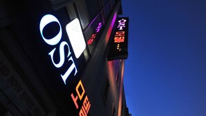 Un bâtiment doté d’enseignes lumineuses, dont l’une affiche le mot « OST » et une autre affiche les lettres « OST » et le chiffre « 5 » dans des couleurs différentes.