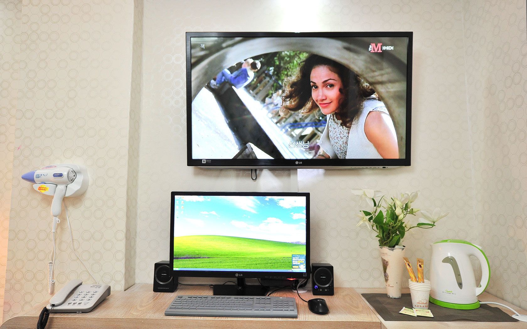 A home office setup with two monitors, a desk phone, a keyboard, a mouse, a speaker, a hairdryer, and a kettle.
