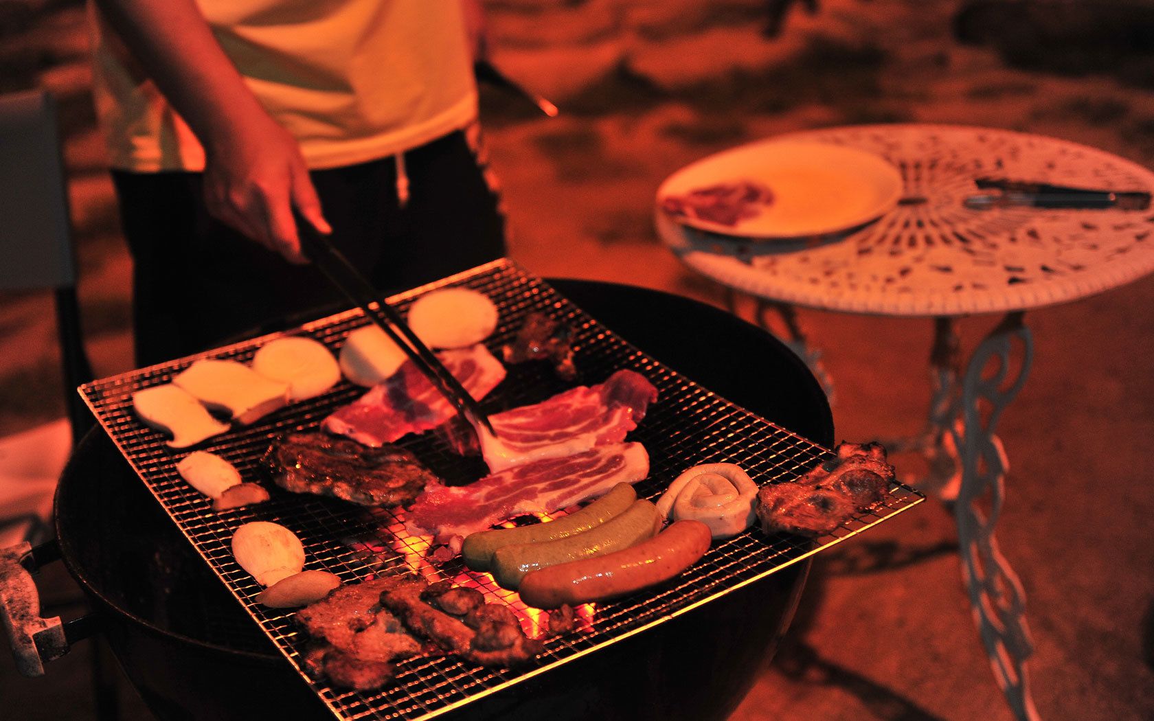 Una parrilla con diversos tipos de carne y salchichas cocinándose al aire libre.