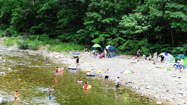 Un terrain de camping au bord de la rivière, avec des tentes et des personnes pratiquant des activités nautiques.