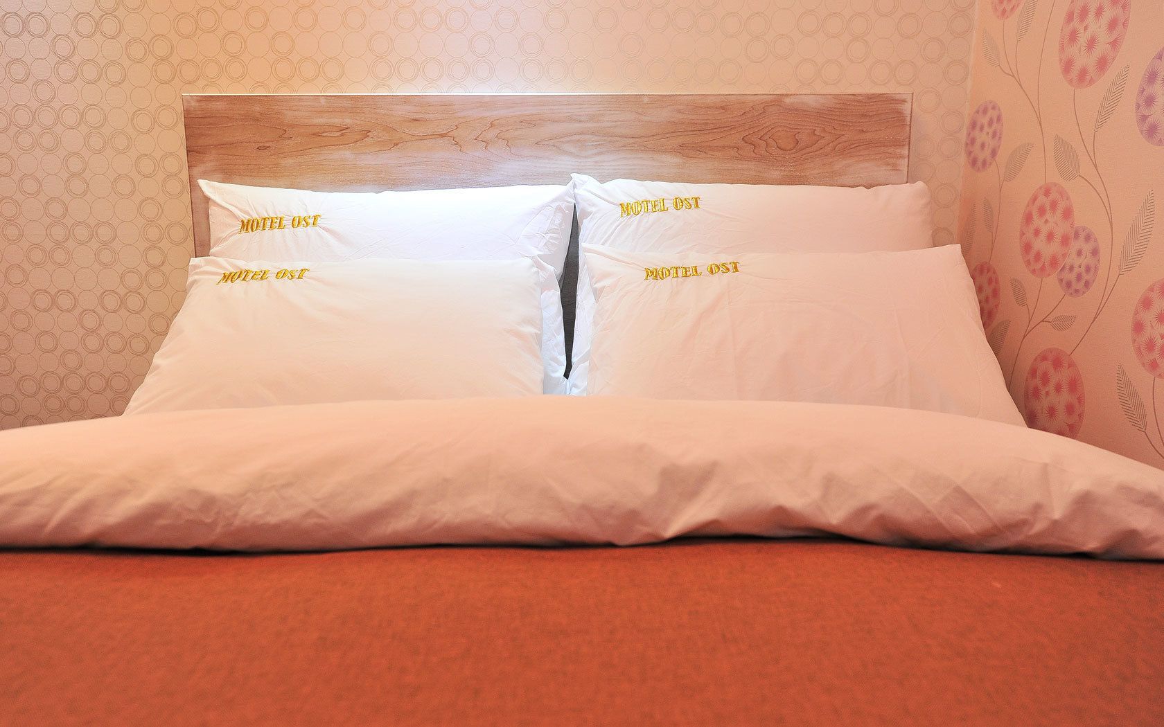 En snyggt bäddad säng med vita sängkläder och kuddar märkta med texten "Motel OST".