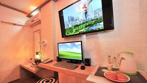 Une chambre d’hôtel équipée d’un bureau, de deux écrans, d’un clavier, d’une souris, d’un haut-parleur, d’une machine à café et d’une assiette de nourriture.