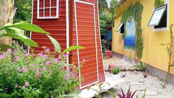Un edificio rojo y amarillo con una estructura de molino, rodeado de plantas en macetas y un jardín.