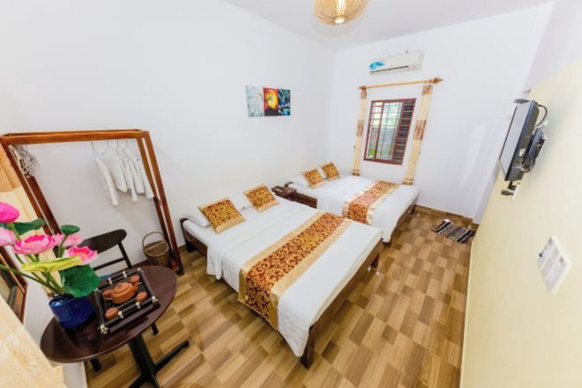 Una habitación con dos camas, piso de madera, una mesa con un jarrón de flores y un aire acondicionado instalado en la pared.