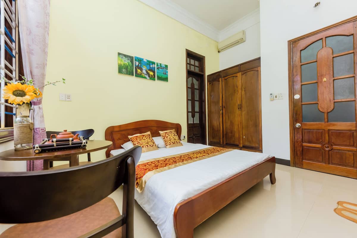 A bedroom with a bed, wooden wardrobe, a table with a chair, and a window with curtains.
