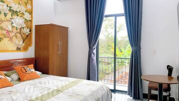 Habitación de hotel con cama, armario de madera, balcón y vistas a zonas verdes, además de aire acondicionado.