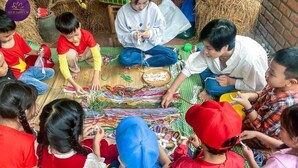 Eine Gruppe Kinder ist in einer Bastelaktivität beschäftigt und sitzt auf einer Matte, vor ihnen liegen verschiedene farbenfrohe Materialien.