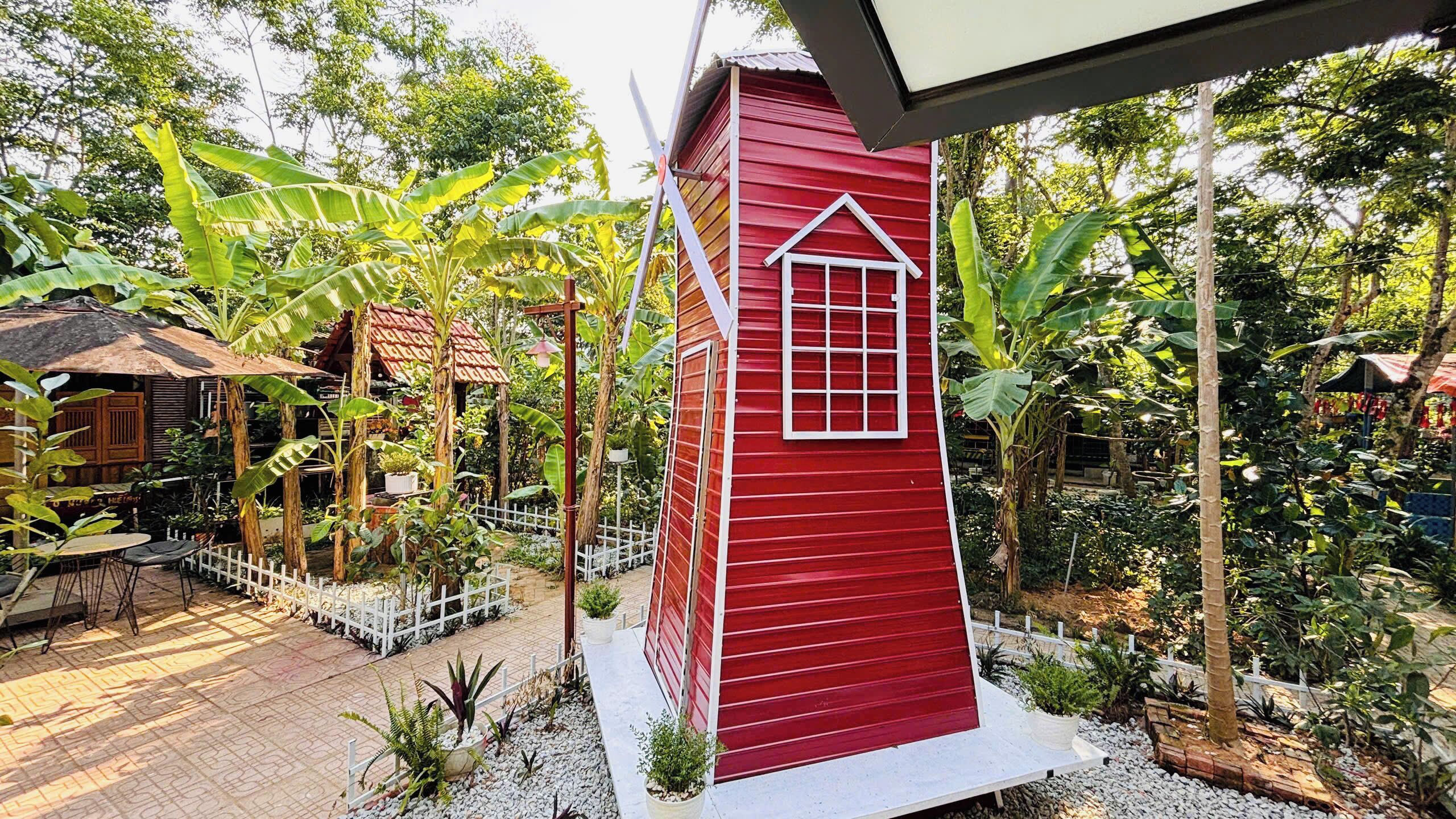 Een rood gebouw met een wit raam en een witte hekken rondom een tuin met verschillende planten en een terras.