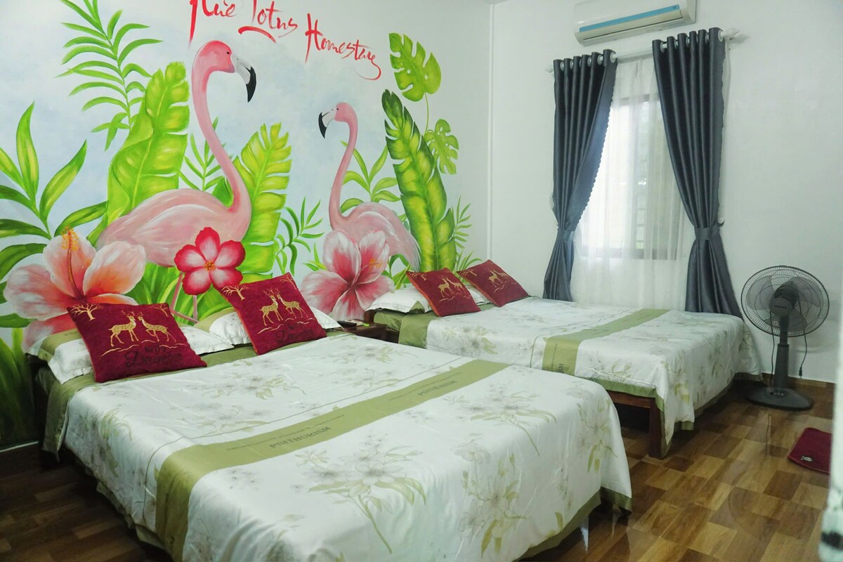A room with two beds, a wall mural, a window with curtains, and a standing fan.