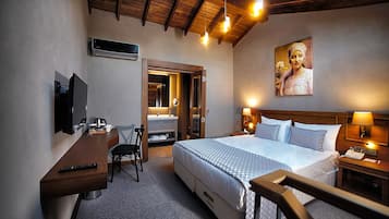 Ein Hotelzimmer mit einem Bett, einem Schreibtisch mit Stuhl, einem Fernseher, einem Badezimmer mit Spiegel und einem Bild an der Wand.