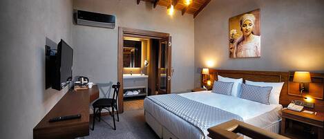 A hotel room with a bed, a desk with a chair, a TV, a bathroom with a mirror, and a painting on the wall.