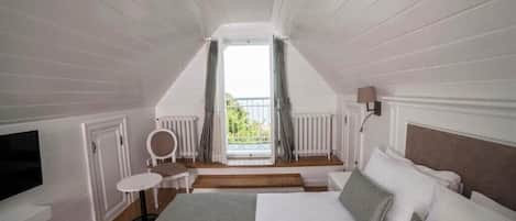 A bedroom with a bed, a small table, a chair, a TV, and a window with curtains.
